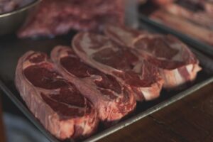 Three beef steaks with visibly different marbling arranged beside USDA-style grade cards on a cutting board.