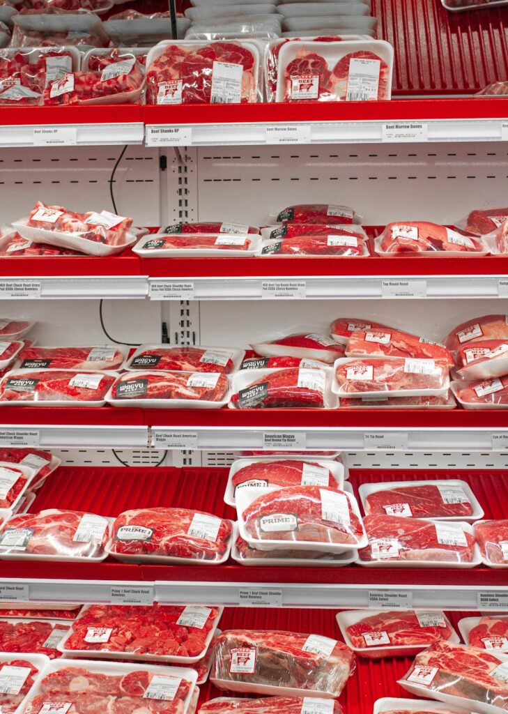 A home cook places sealed raw meat on the lowest refrigerator shelf beside an appliance thermometer.