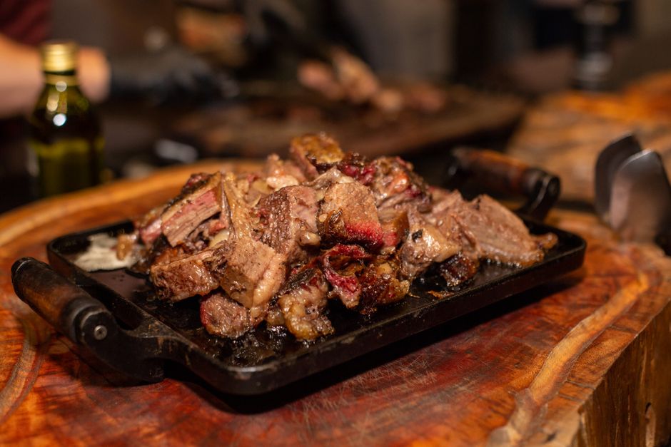 A cook uses a meat thermometer to check a thick steak beside several fresh beef cuts on a wooden counter.